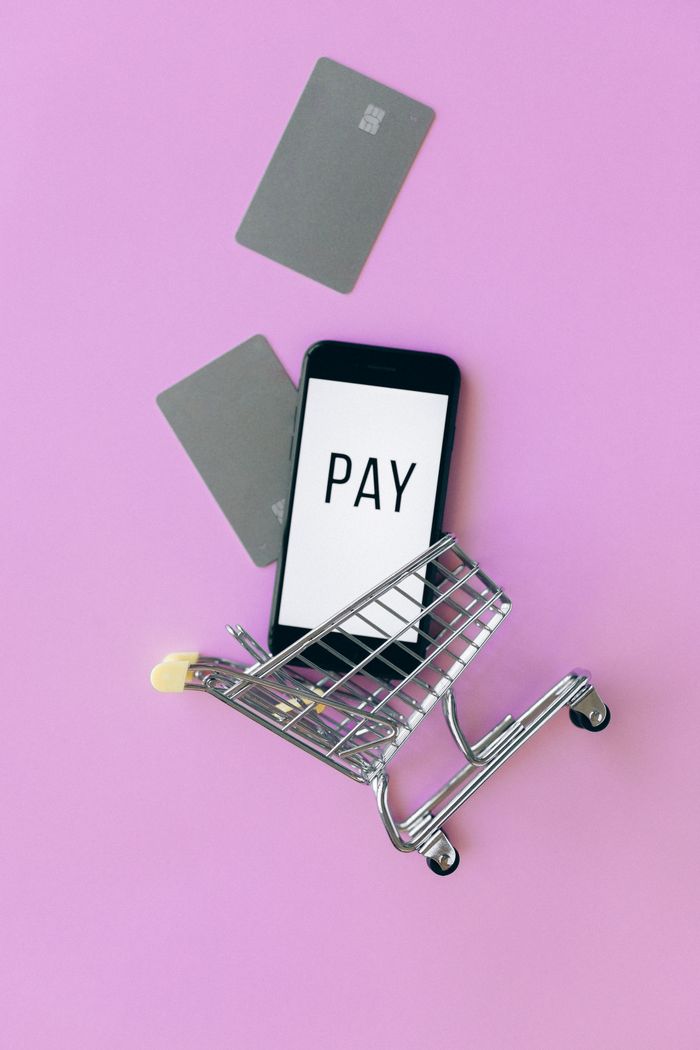 Top view of a smartphone in a shopping cart with credit cards on a purple background.